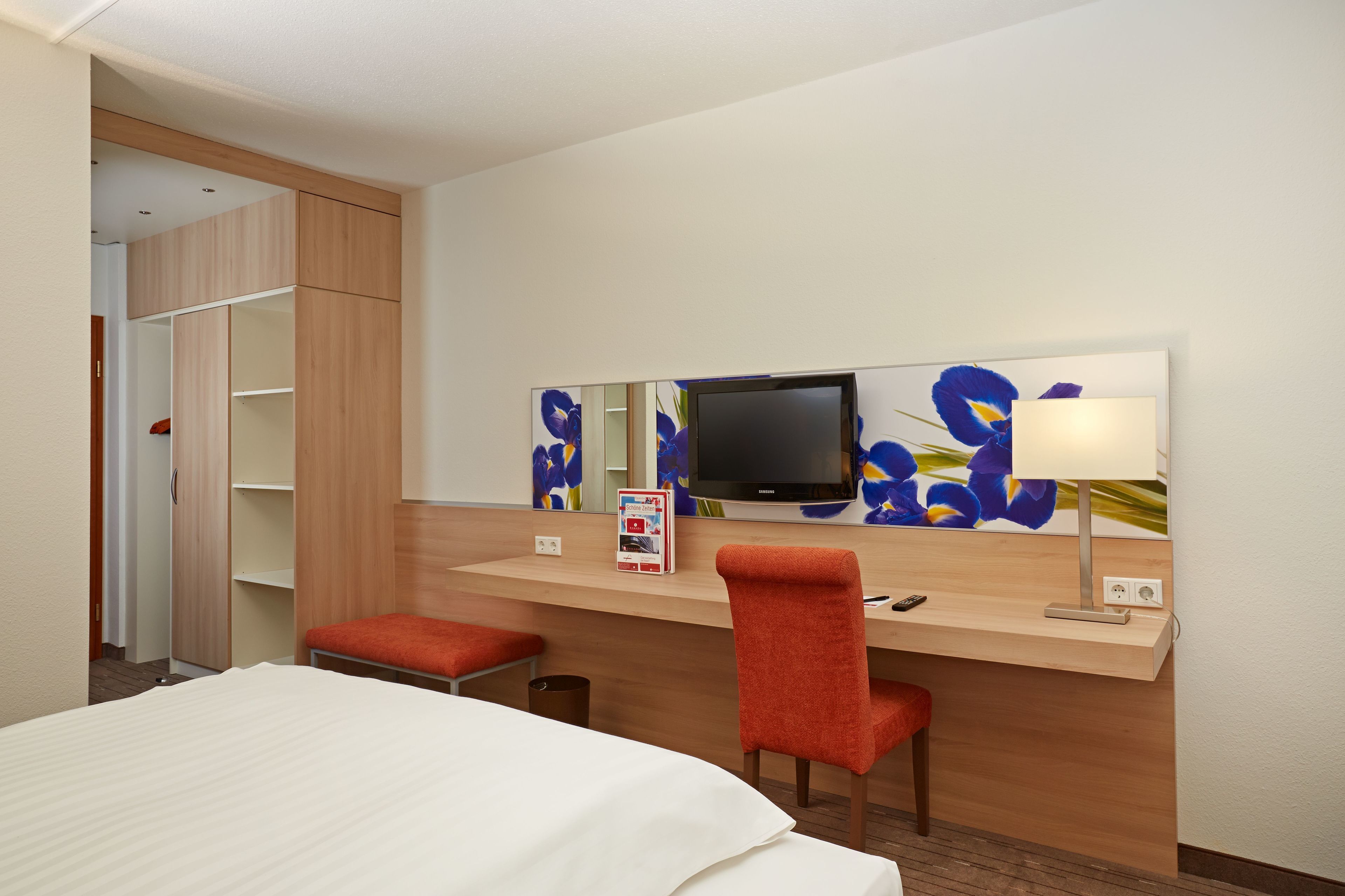 Una habitación de hotel con cama, escritorio, silla, televisor y espejo.