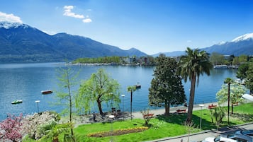 A lakeside view with mountains, a marina, and a park with benches and trees.