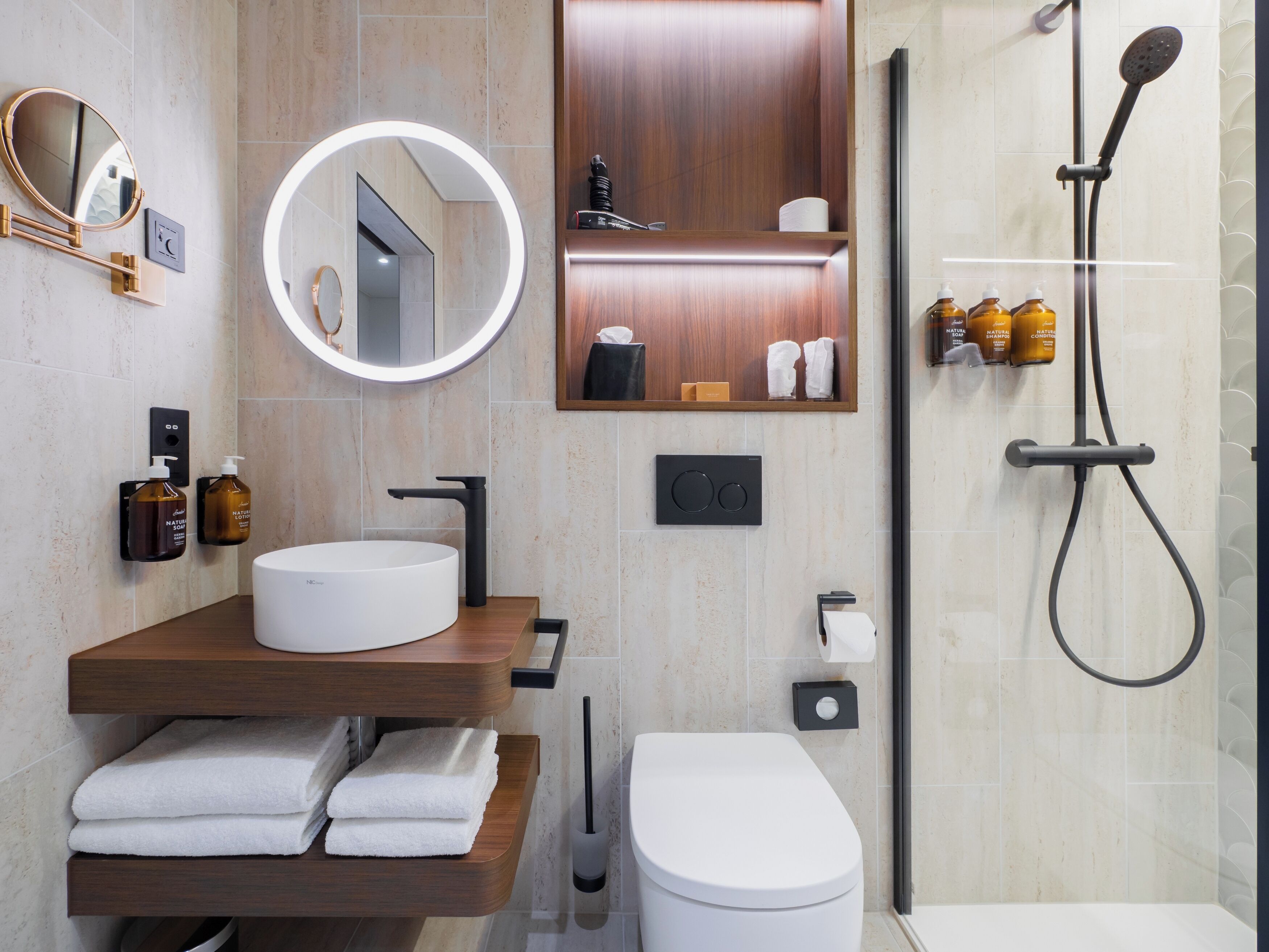 A modern bathroom with a round mirror, a white sink, a toilet, and a shower area.