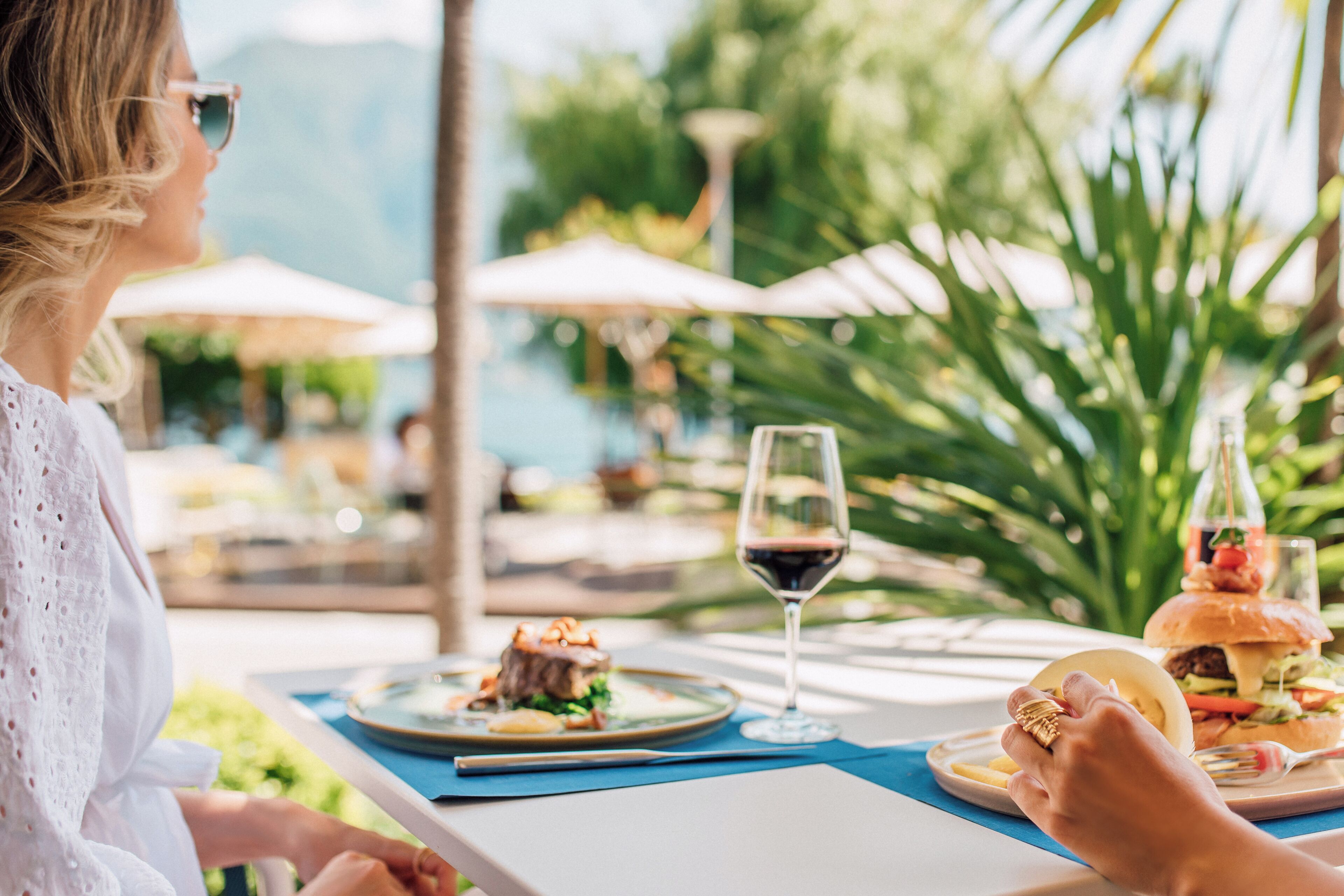 Ein Esstisch mit einem Teller Essen, einem Glas Rotwein und einem Hamburger.