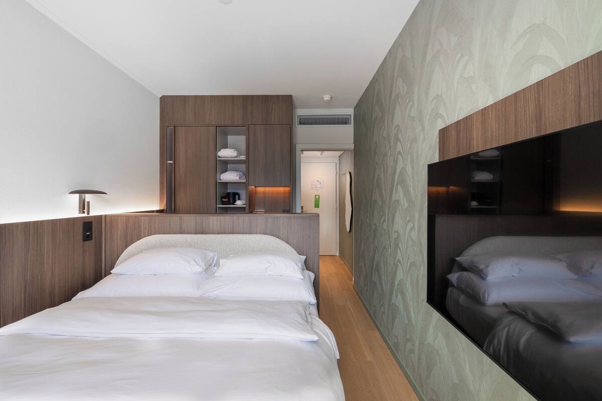 A modern hotel room with a large bed, built-in wardrobe, and a mirror.