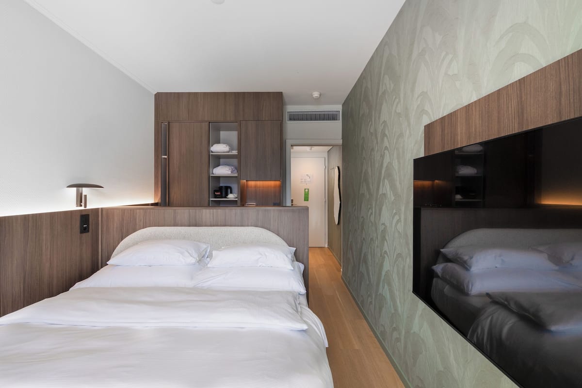 Una habitación de hotel moderna con una cama grande, armario empotrado y un espejo.