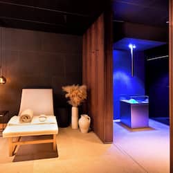 Relax in a serene spa room with a wooden bench, side table, and soothing blue-lit ambiance.