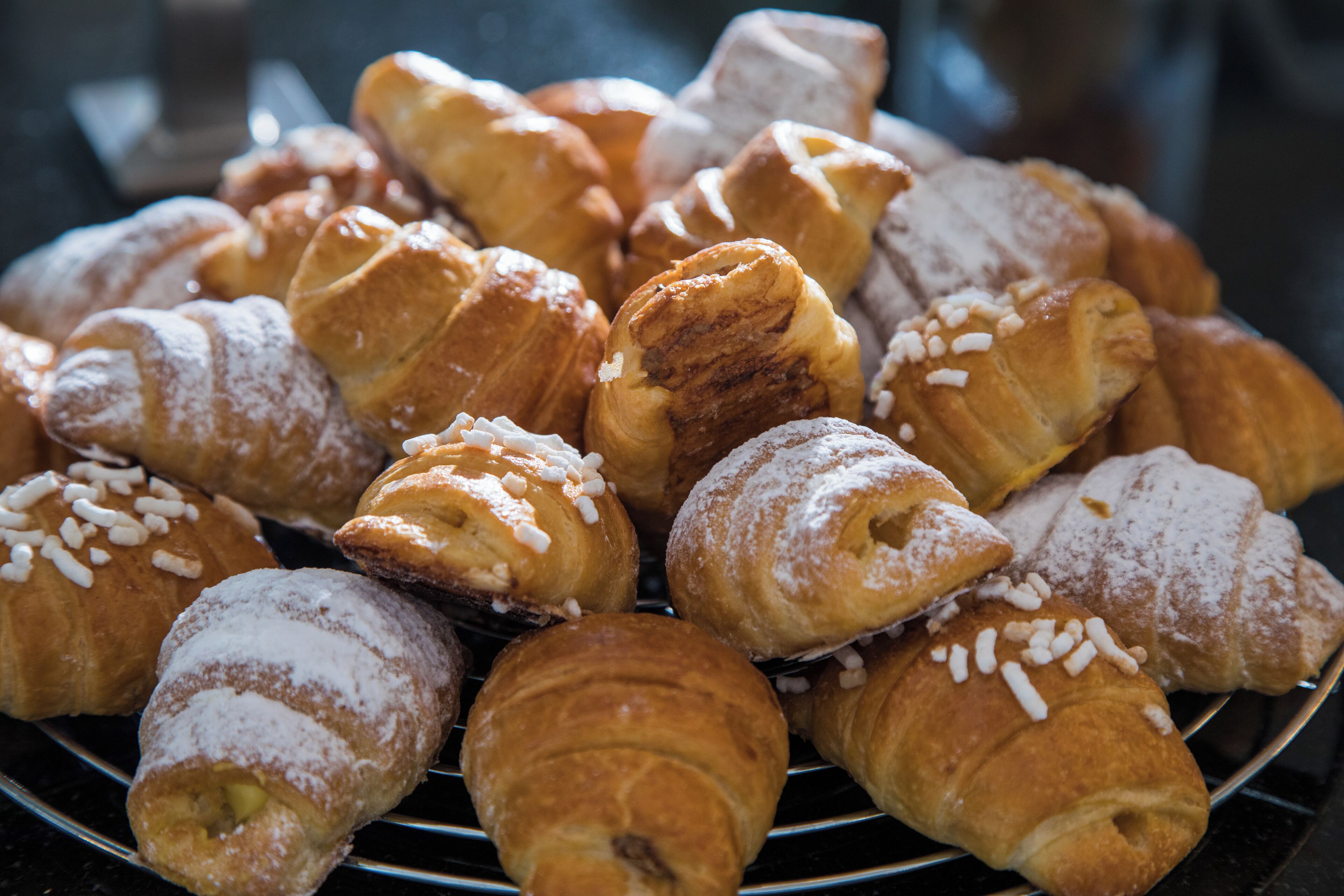 Une variété de viennoiseries, notamment des croissants et des pains au chocolat, disposées sur une grille métallique.