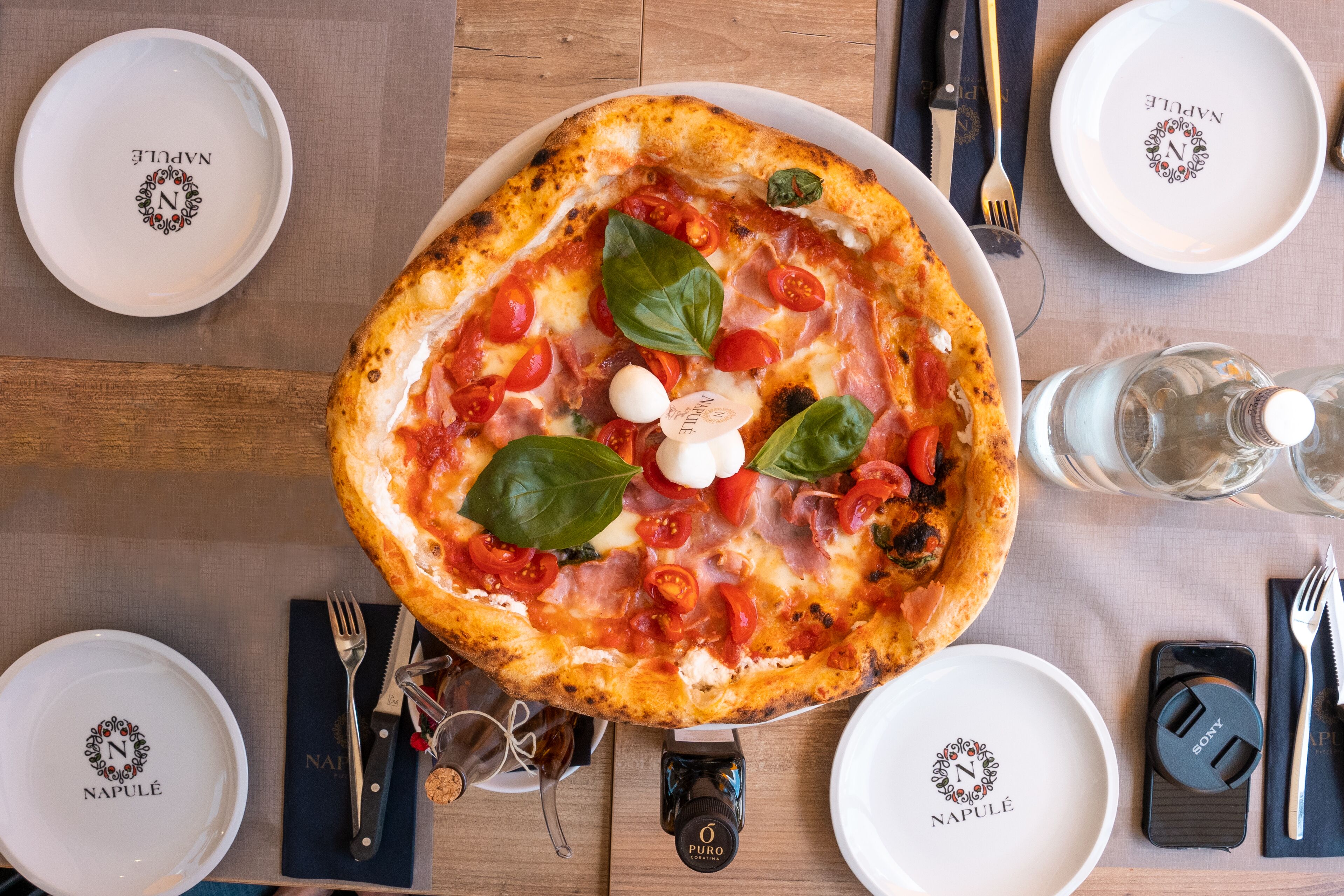 Une pizza sur une table en bois, avec une serviette, une fourchette, un couteau et des verres.