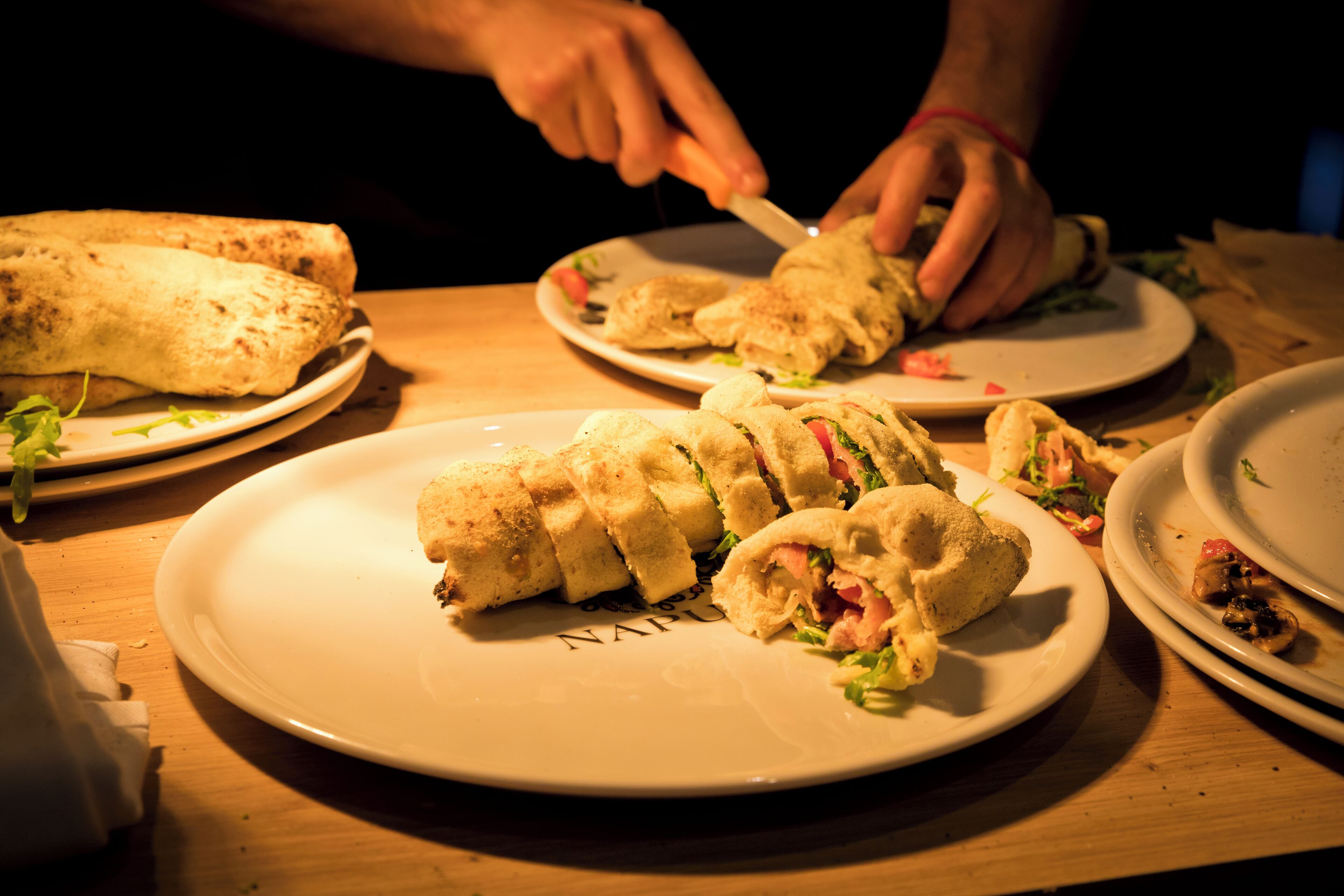 Une table à manger avec plusieurs assiettes remplies de nourriture, notamment des sandwichs et un plat enroulé, probablement un burrito ou un wrap.