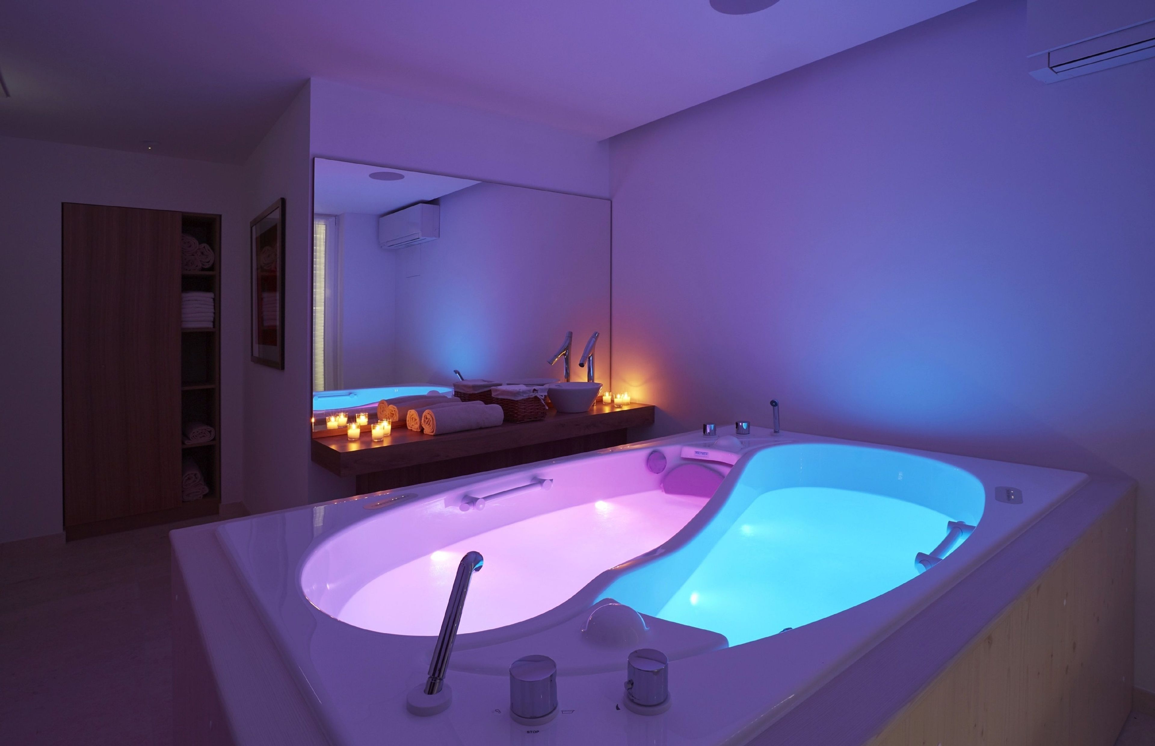 A modern bathroom with a large bathtub, a wooden cabinet, and a mirror reflecting the room.