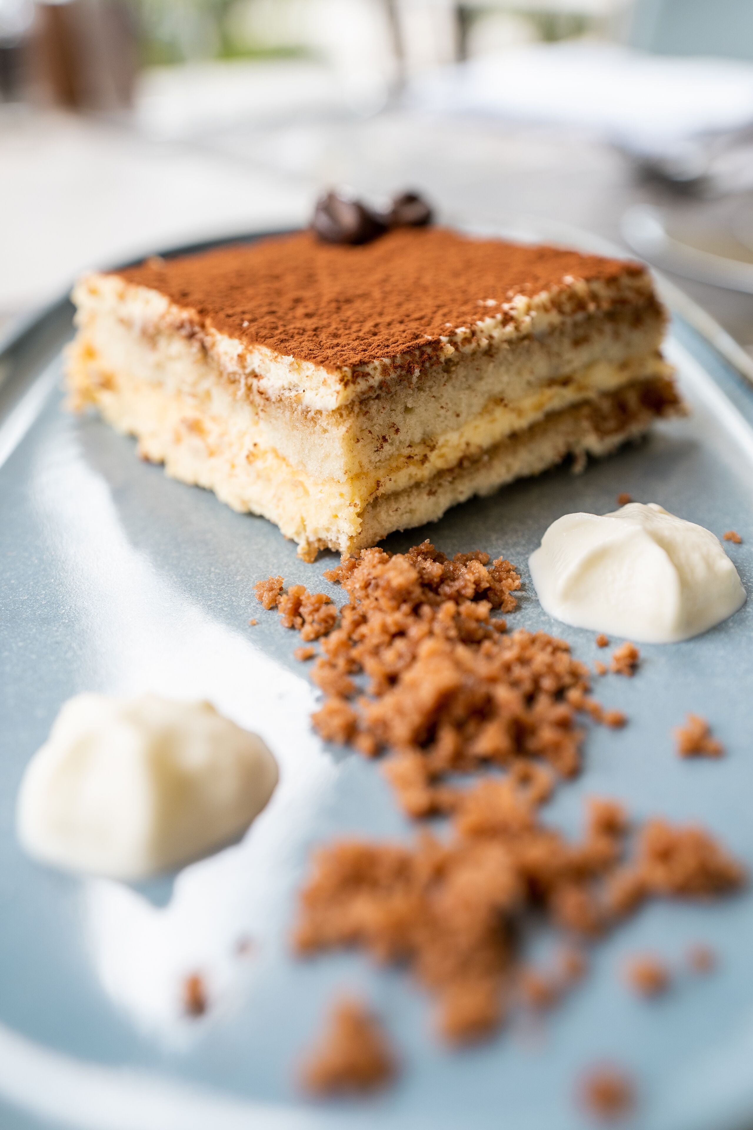 Ein Stück Tiramisu auf einem Teller, mit Krümeln und Sahnetupfen.