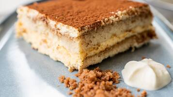 Ein Stück Tiramisu auf einem Teller, mit Krümeln und Sahnetupfen.