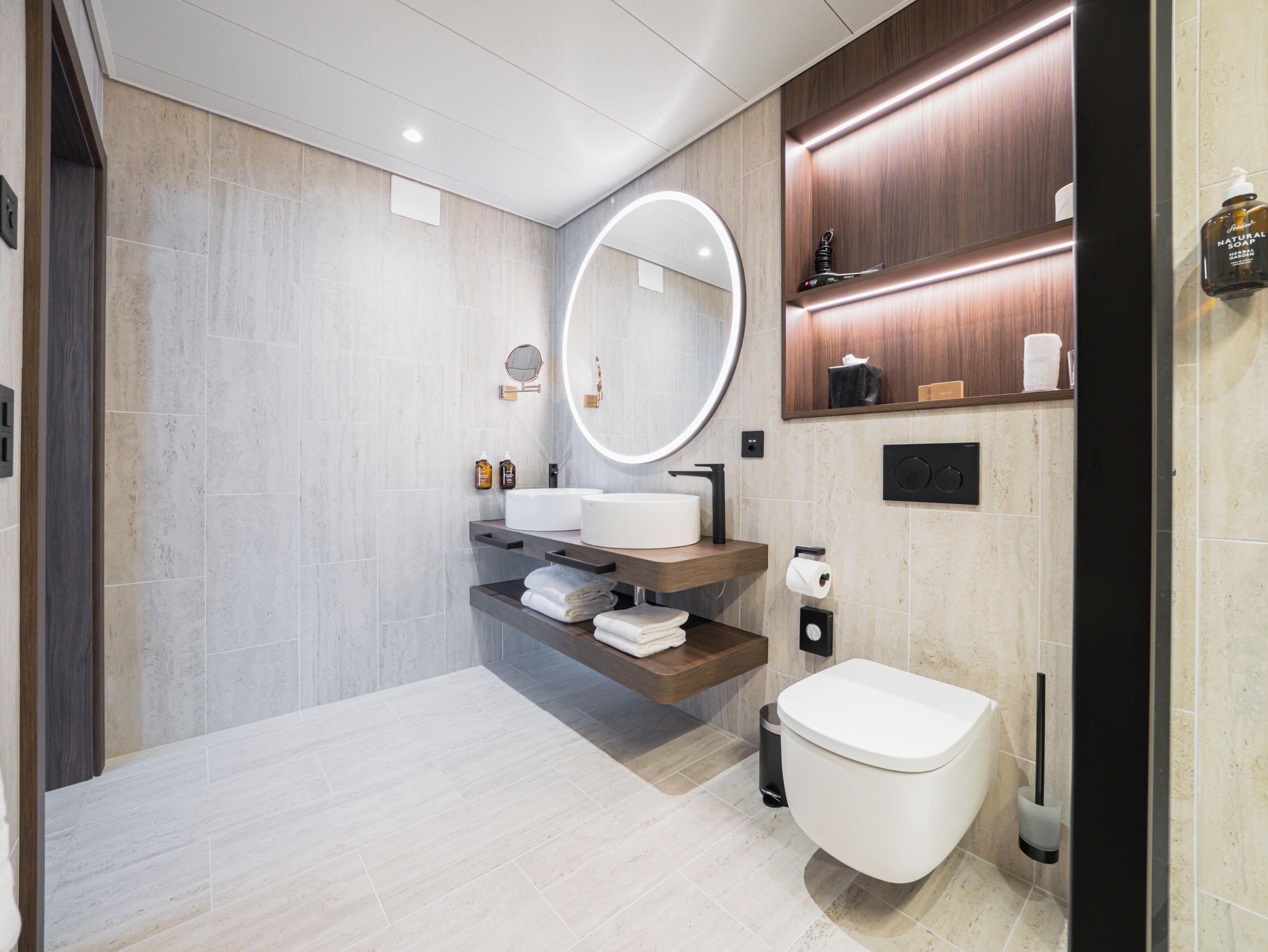 A modern bathroom with a large mirror, a toilet, a sink, and a shelf with toiletries.
