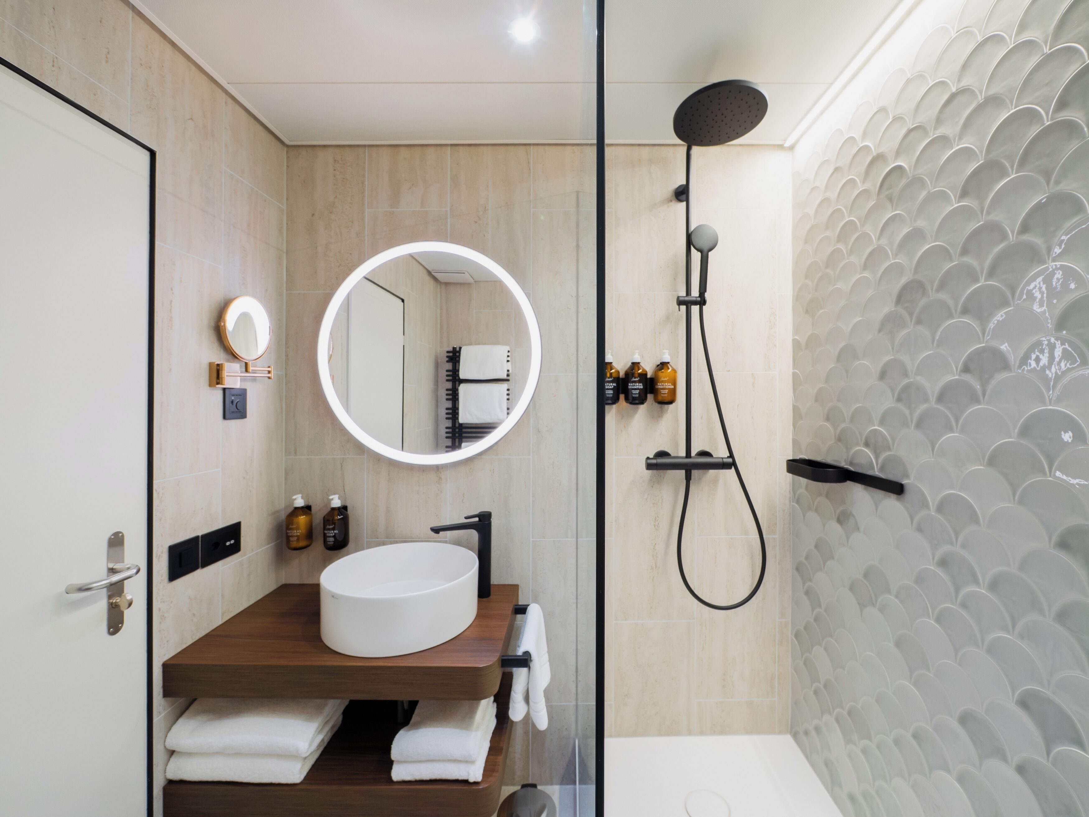 A modern bathroom with a round mirror, a sink, a handheld showerhead, and a towel rack.