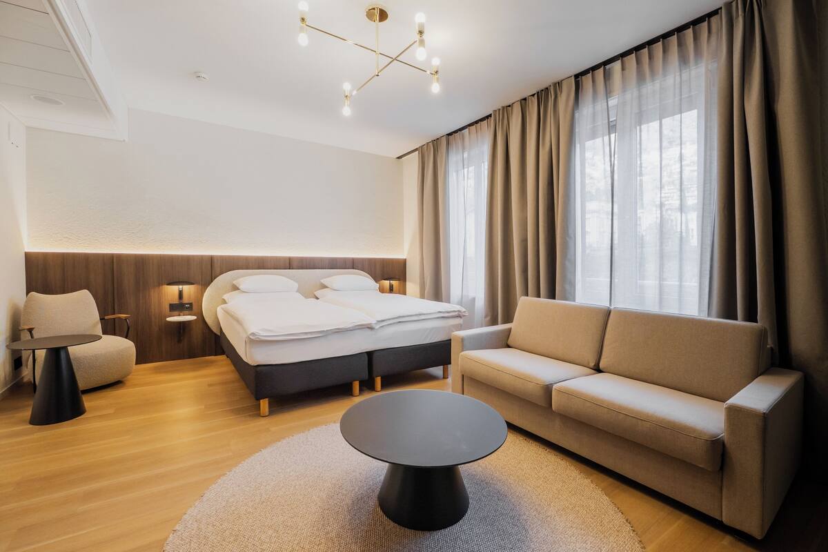 A modern hotel room with a bed, sofa, round coffee table, and a chandelier.