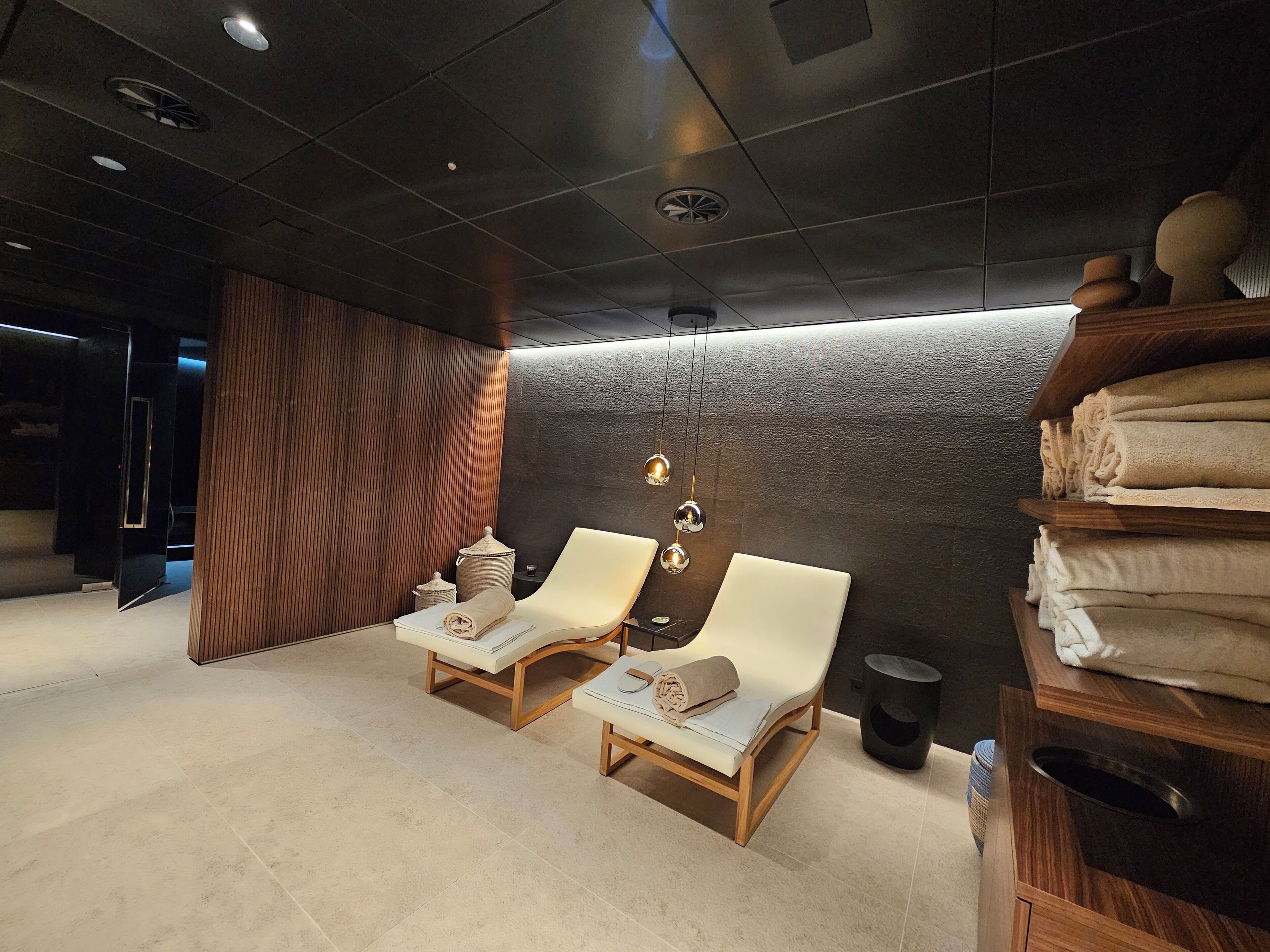 Ein moderner Wellnessraum mit zwei Liegesesseln, einer strukturierten Wand und einem Stapel Handtüchern.
