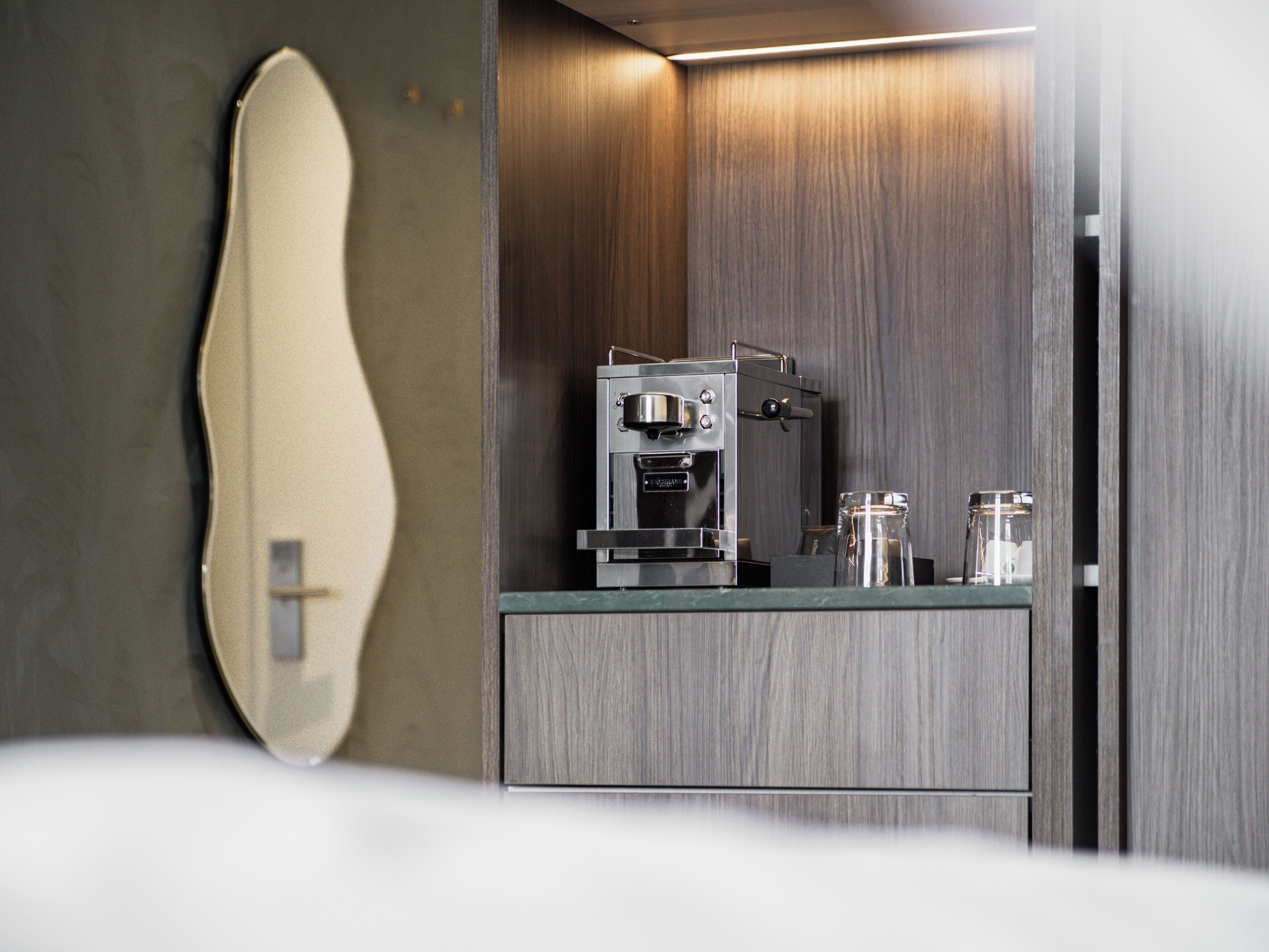 Een moderne badkamer met een houten wastafel, een ingebouwde koffieapparaat en een grote spiegel.