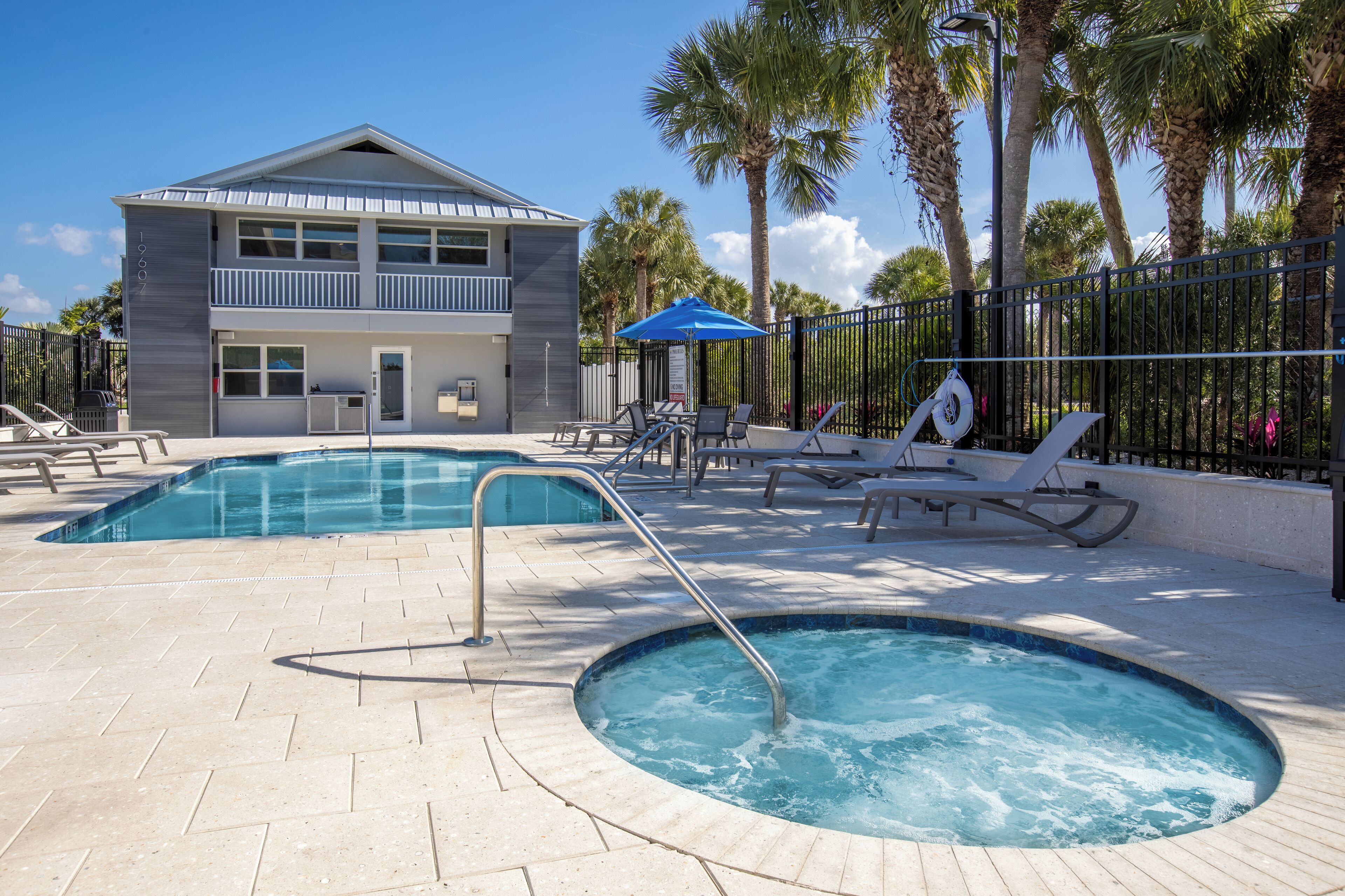 A pool area with a hot tub, lounge chairs, and a building with a balcony.