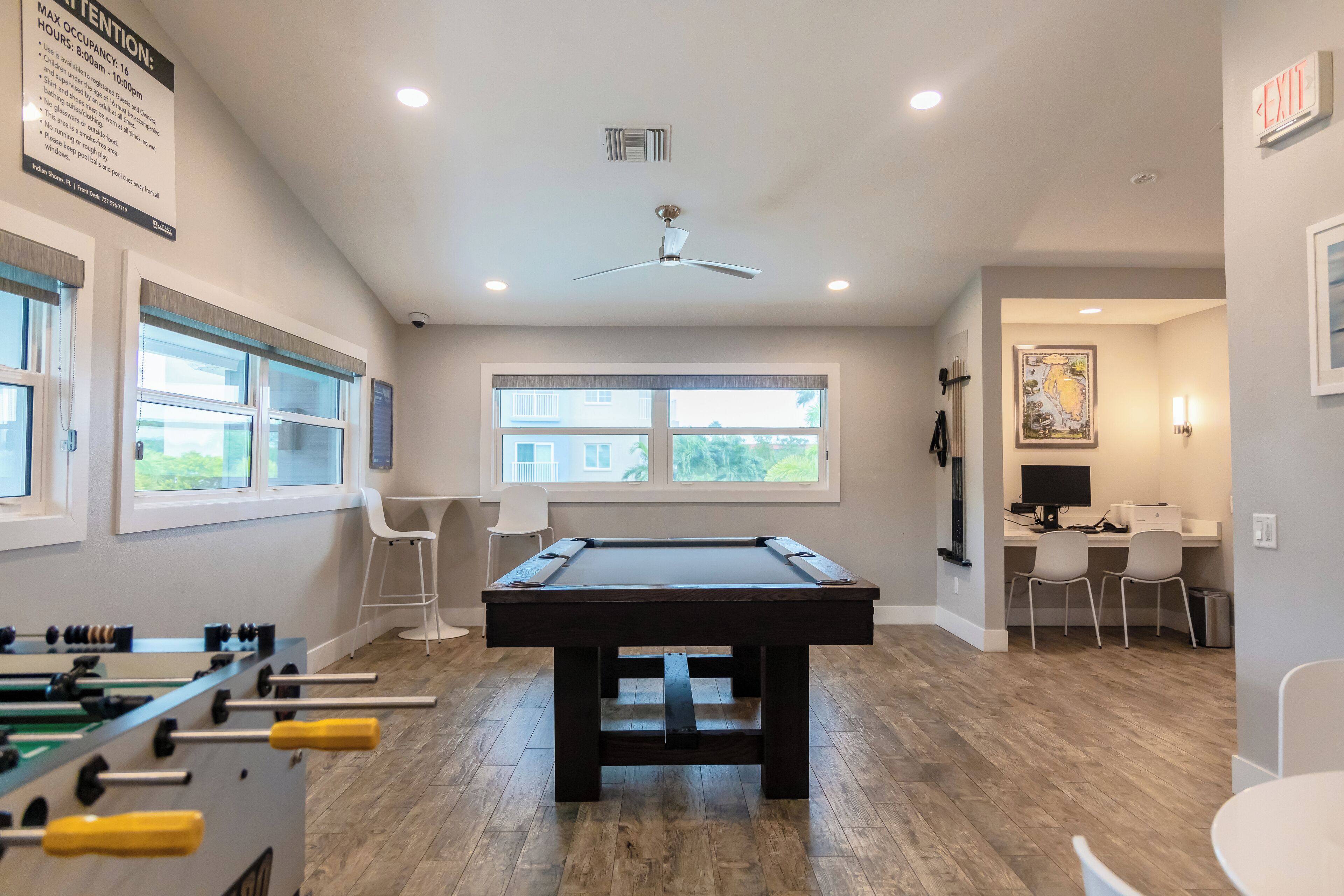 A pool table in a room with a ceiling fan, a foosball table, and a desk with chairs.