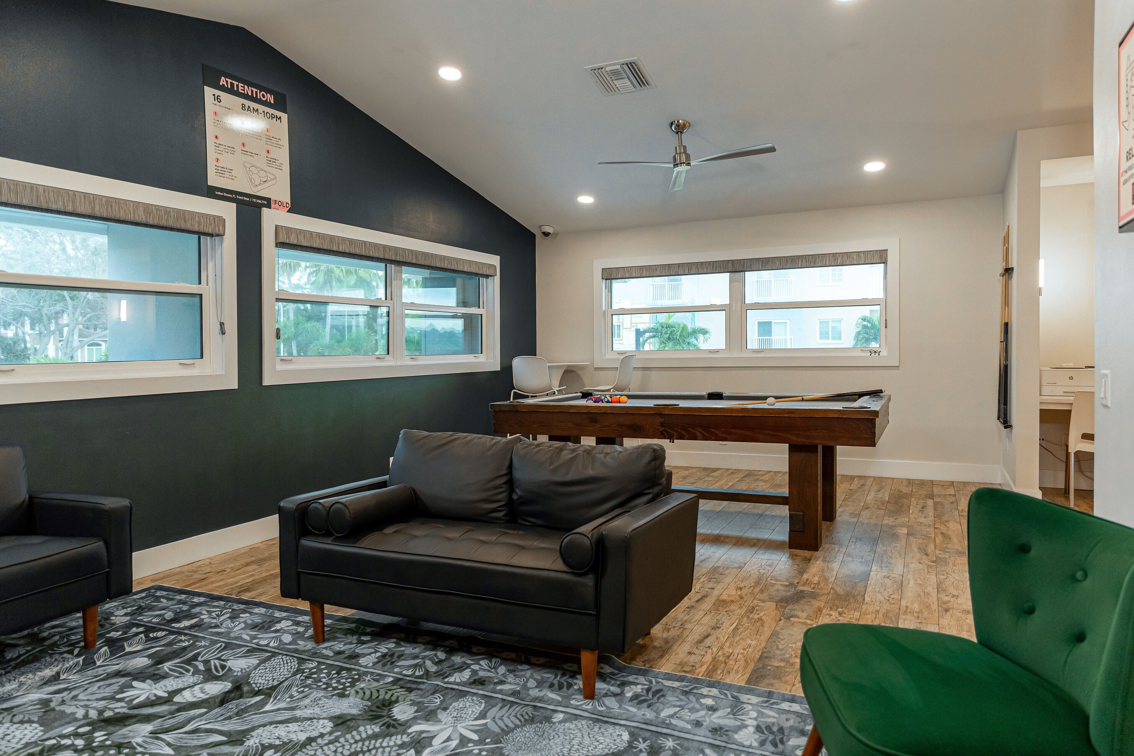 Una habitación con mesa de billar, una silla verde, un sofá de cuero negro y un ventilador de techo.