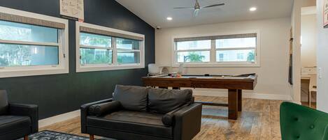 Una habitación con mesa de billar, una silla verde, un sofá de cuero negro y un ventilador de techo.