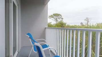 A balcony with two blue and white chairs, a white railing, and a view of greenery and trees.