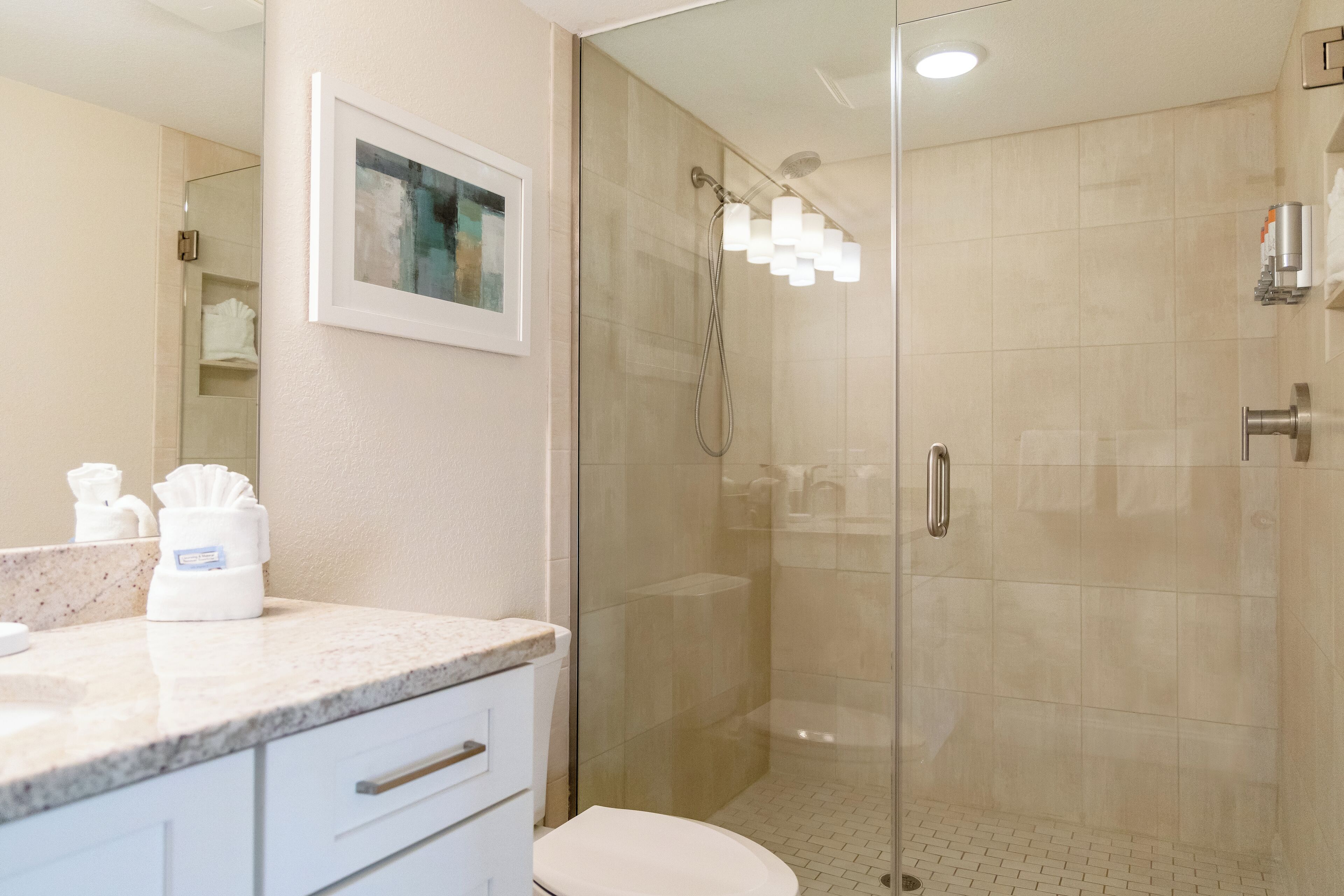 A modern bathroom with a glass-enclosed shower, a marble countertop, and a white toilet.