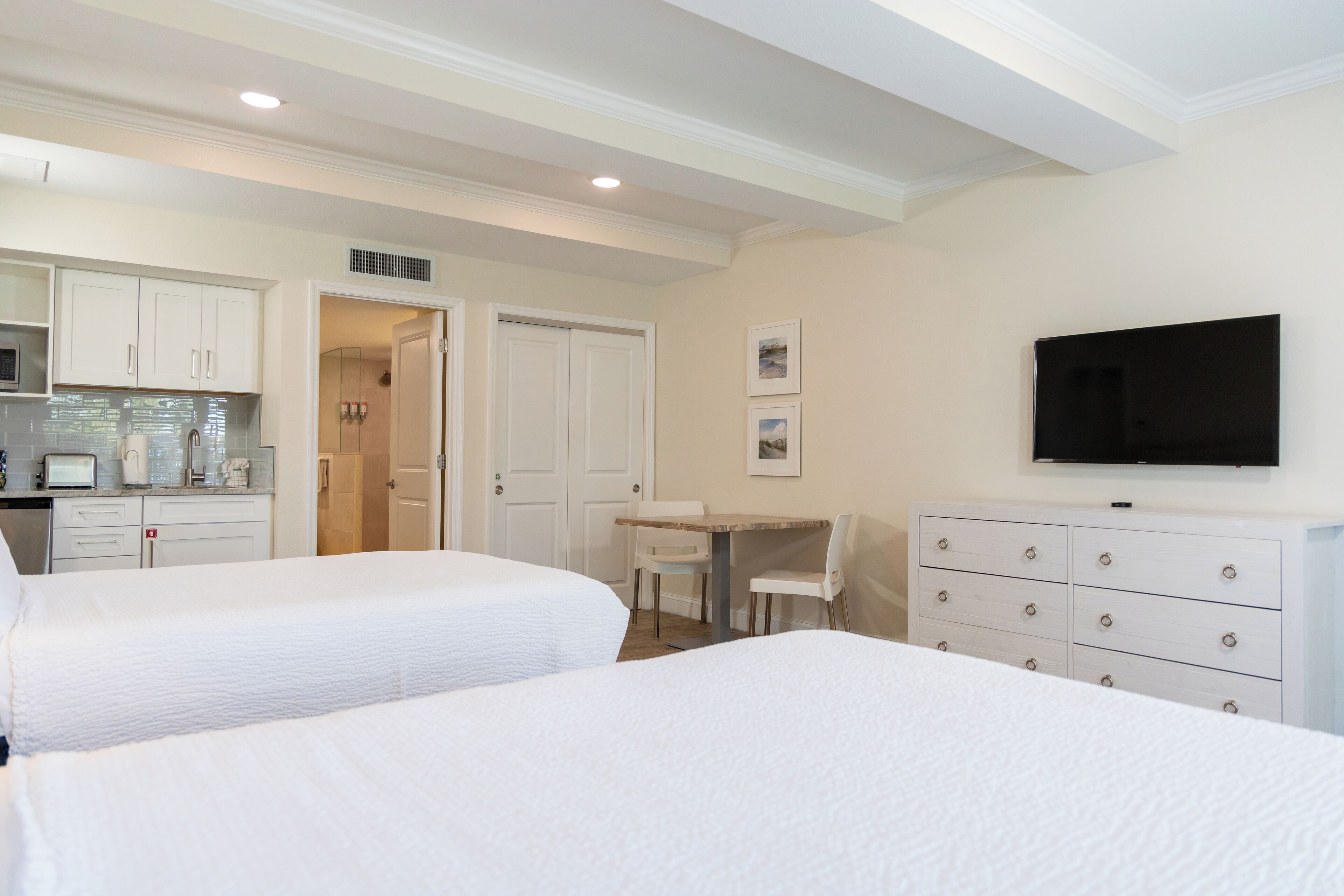 A hotel room with two beds, a desk, a chair, a television, and a kitchenette.