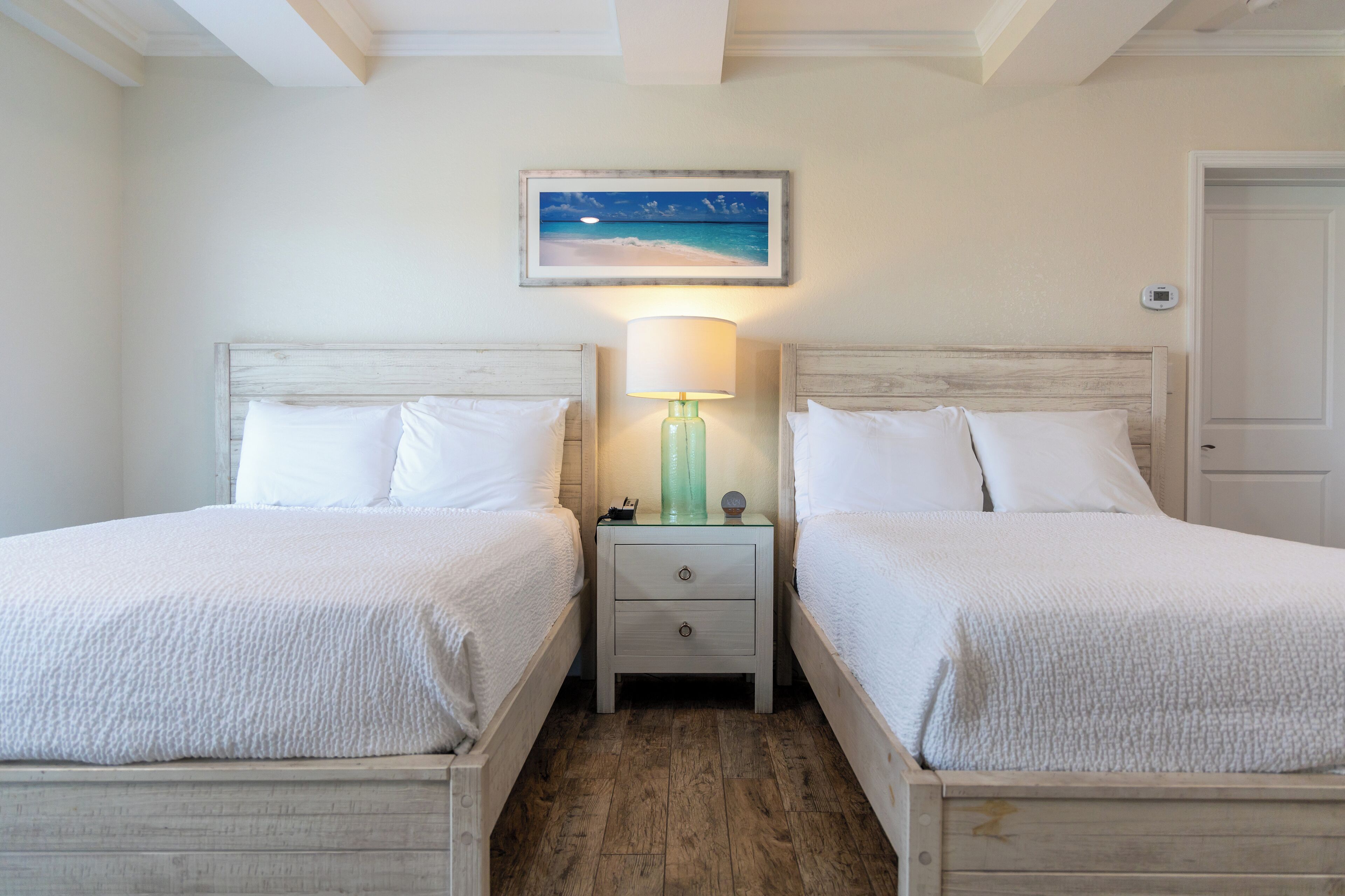 A twin room with two beds, a nightstand with a lamp, and a painting of a beach scene.