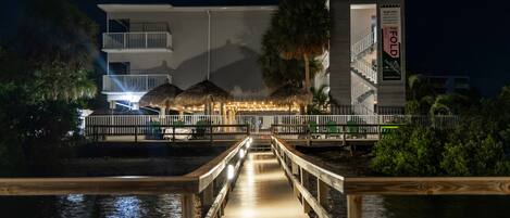 Un muelle de madera que lleva a un hotel con estructura de techo de paja y un letrero que indica que el 80% de la electricidad es producida localmente.