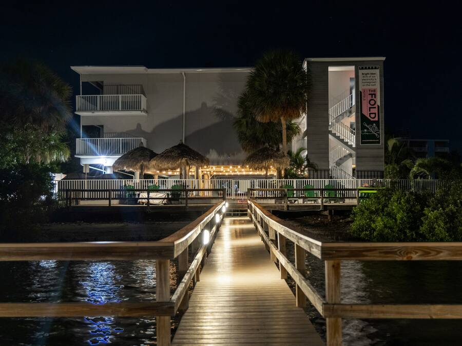 Un muelle de madera que lleva a un hotel con estructura de techo de paja y un letrero que indica que el 80% de la electricidad es producida localmente.