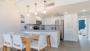 Una cocina moderna con armarios blancos, electrodomésticos de acero inoxidable y una mesa de comedor de vidrio con sillas blancas.