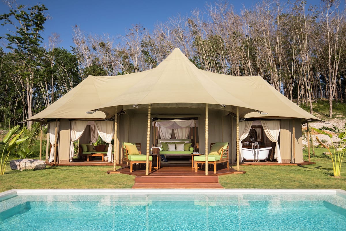 A tented accommodation with a pool, two lounge chairs, a bathtub, and a bed with a canopy.