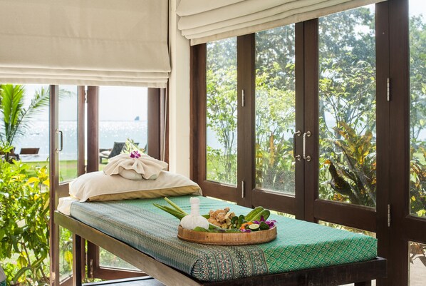 A massage table with a green patterned mat, a white towel, and a basket of herbs and flowers. - Koyao Island Resort (Ko Yao)