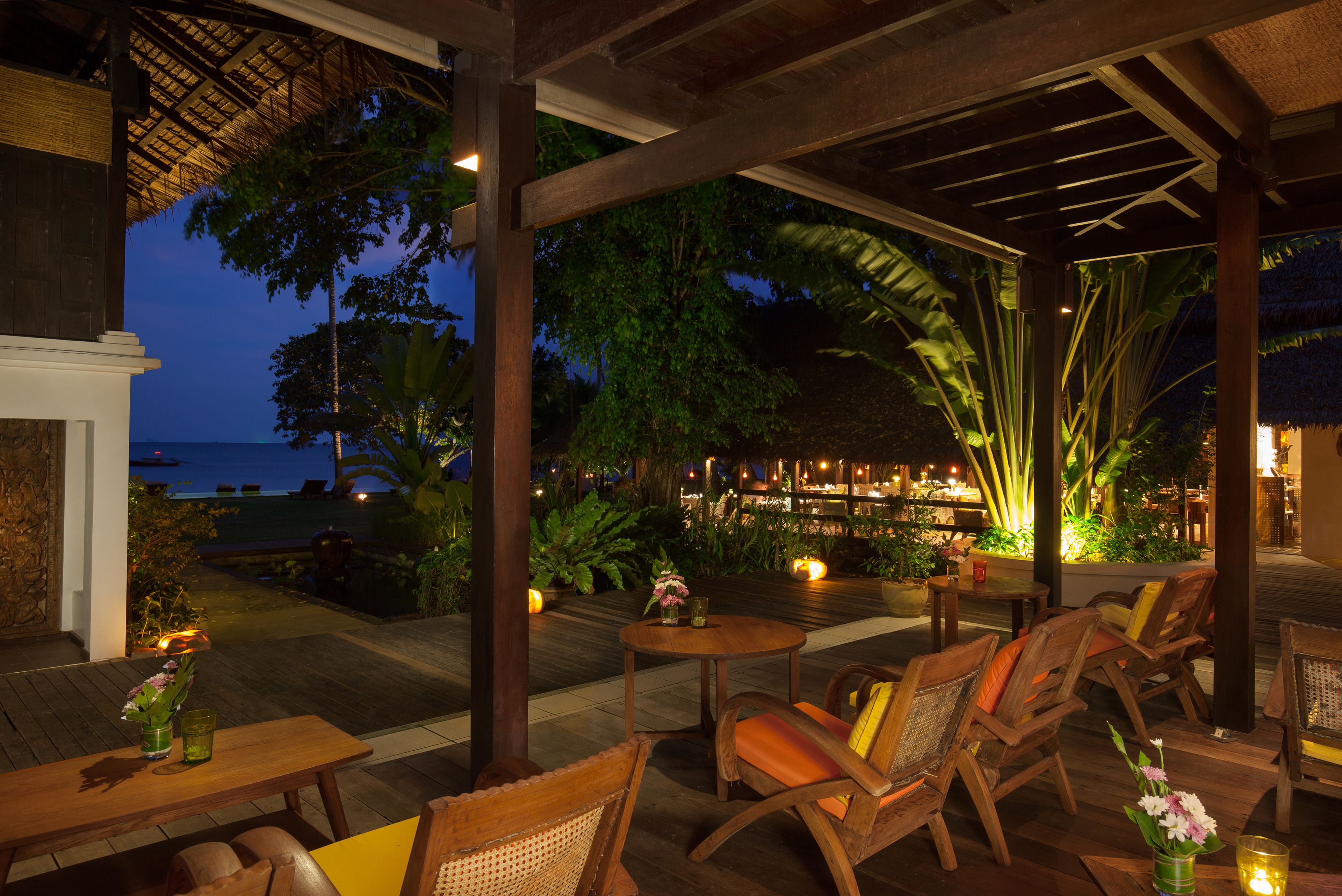 An outdoor seating area with wooden furniture and a view of the ocean at dusk.