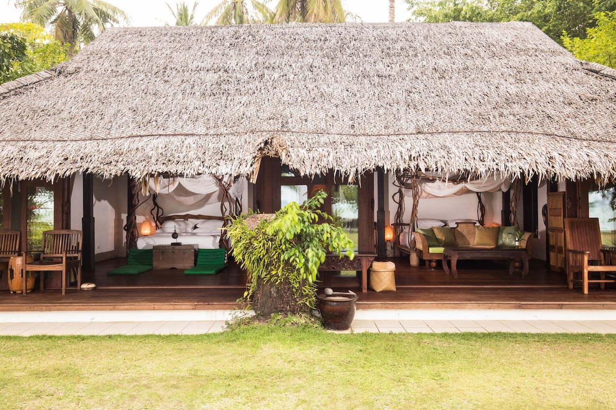 A thatched-roof structure with a bed, seating area, and a small garden.