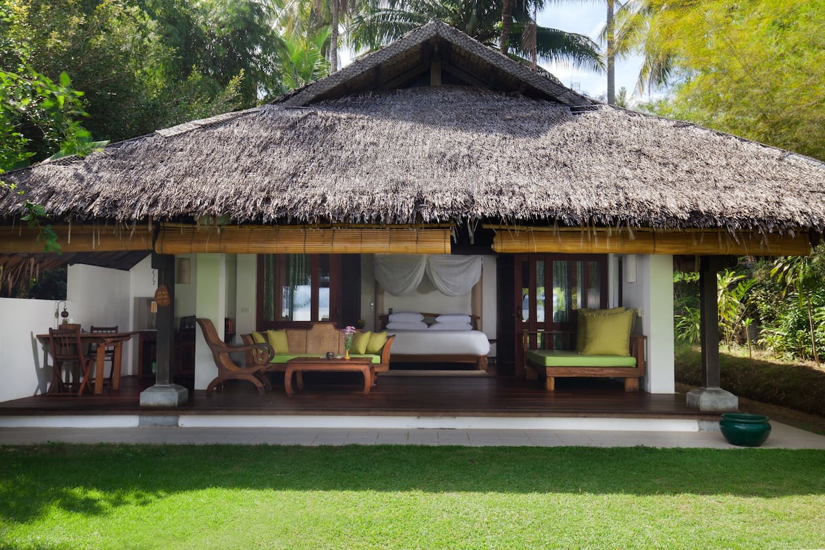 A thatched-roof bungalow with a bed, sofa, and dining area.
