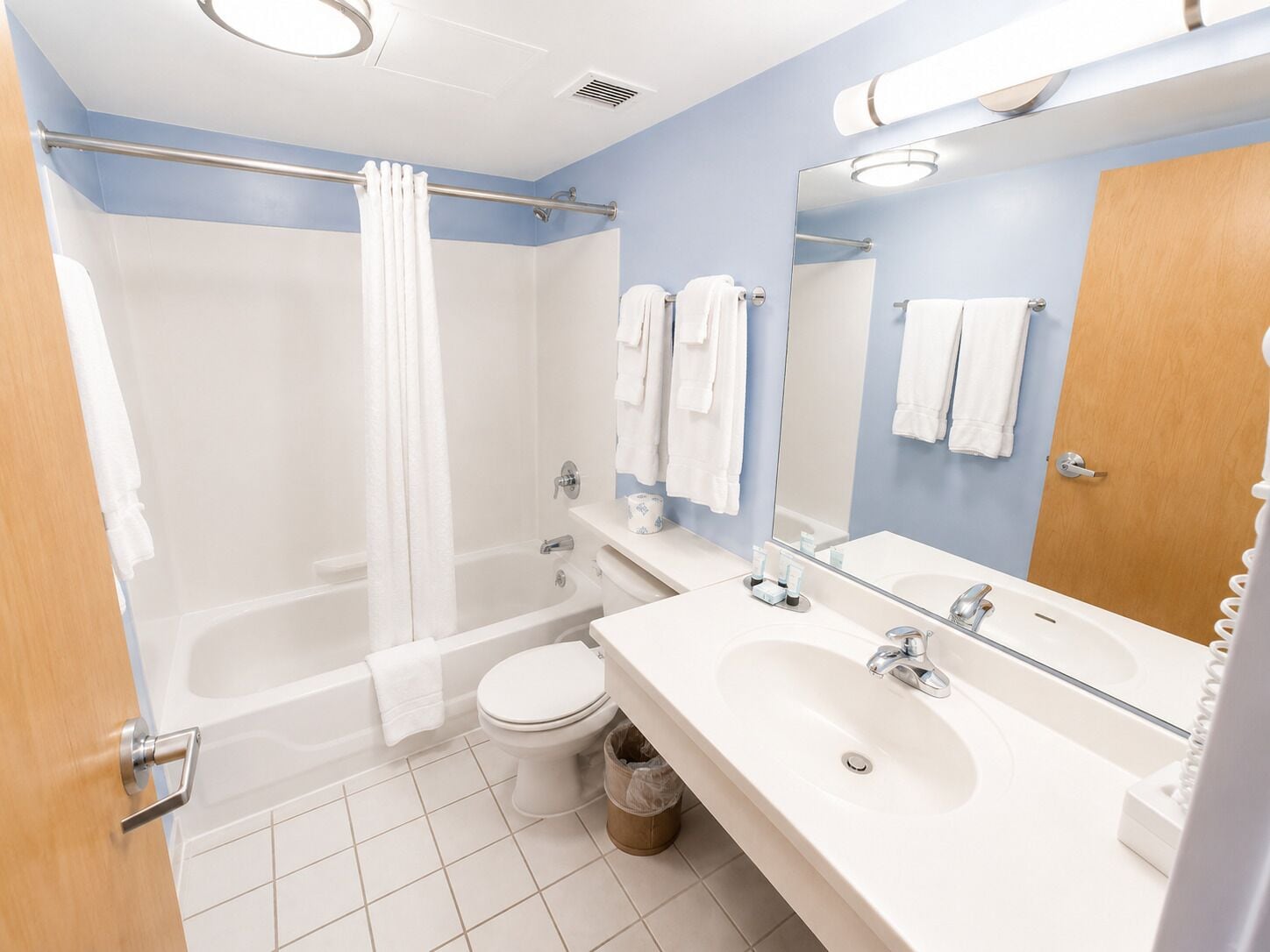 Un baño moderno con bañera, inodoro y lavamanos, que cuenta con un espejo grande y un perchero para toallas.