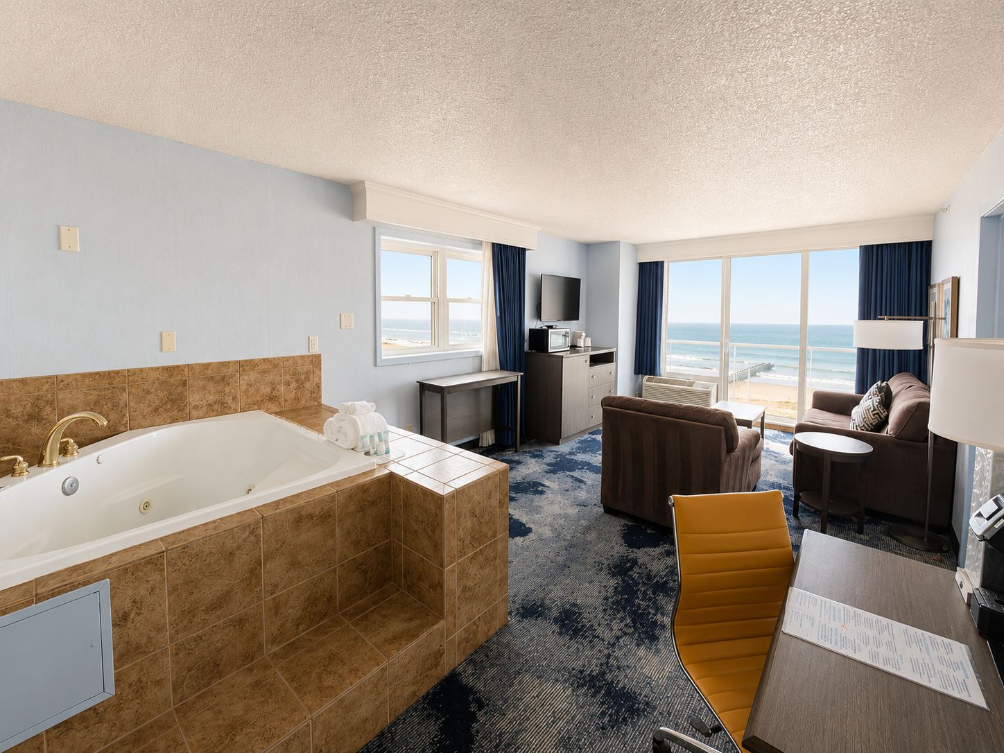 Habitación de hotel con una bañera grande, un sofá, una mesa de comedor y vista a la playa.