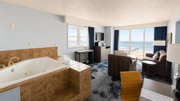 Habitación de hotel con una bañera grande, un sofá, una mesa de comedor y vista a la playa.