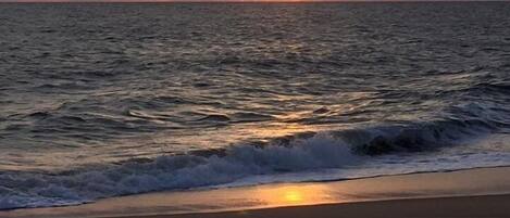 Ein Strand mit Wellen und einem Sonnenuntergang.