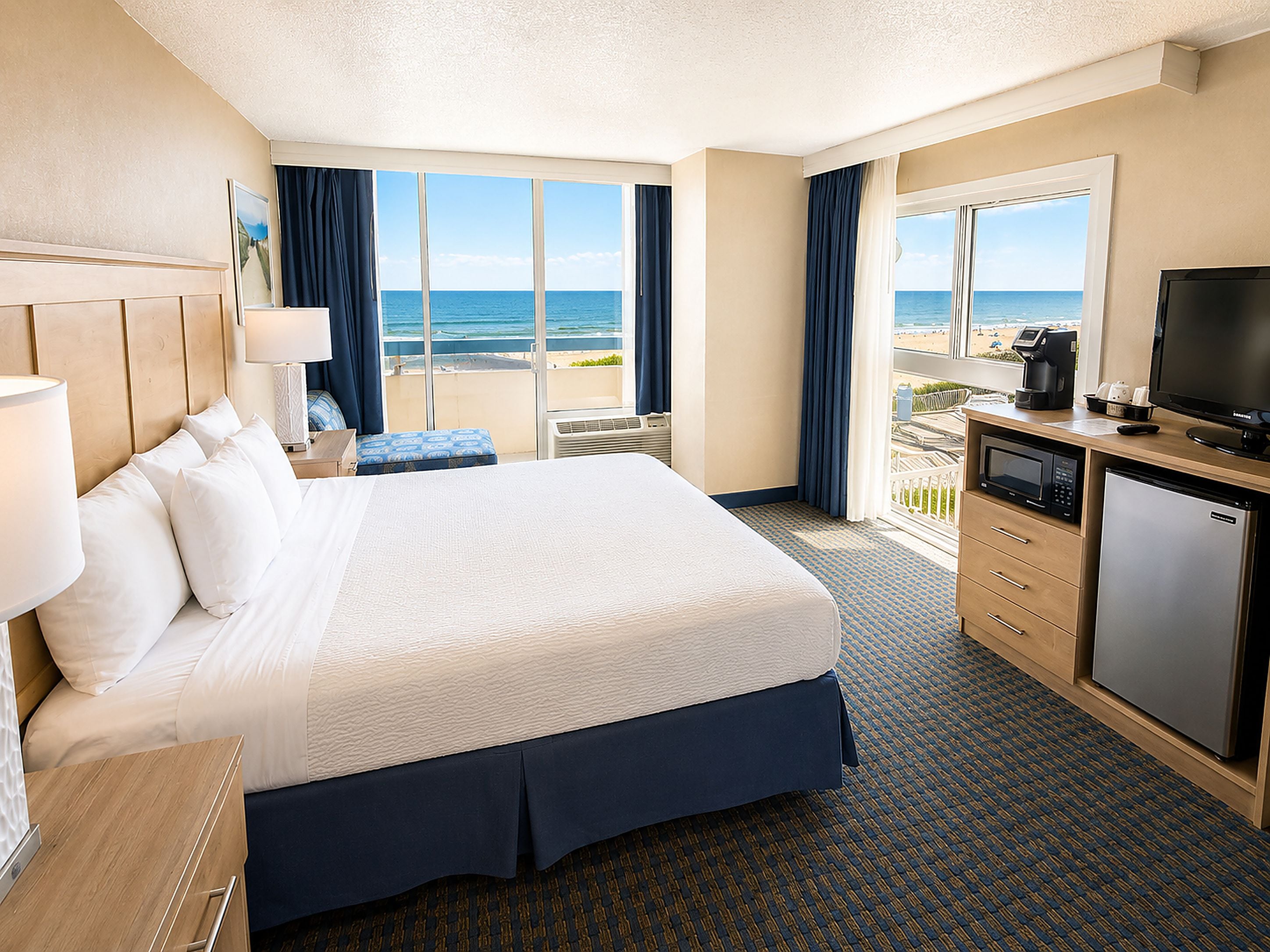 A hotel room with a large bed, a desk with a television, a coffee maker, and a view of the ocean.