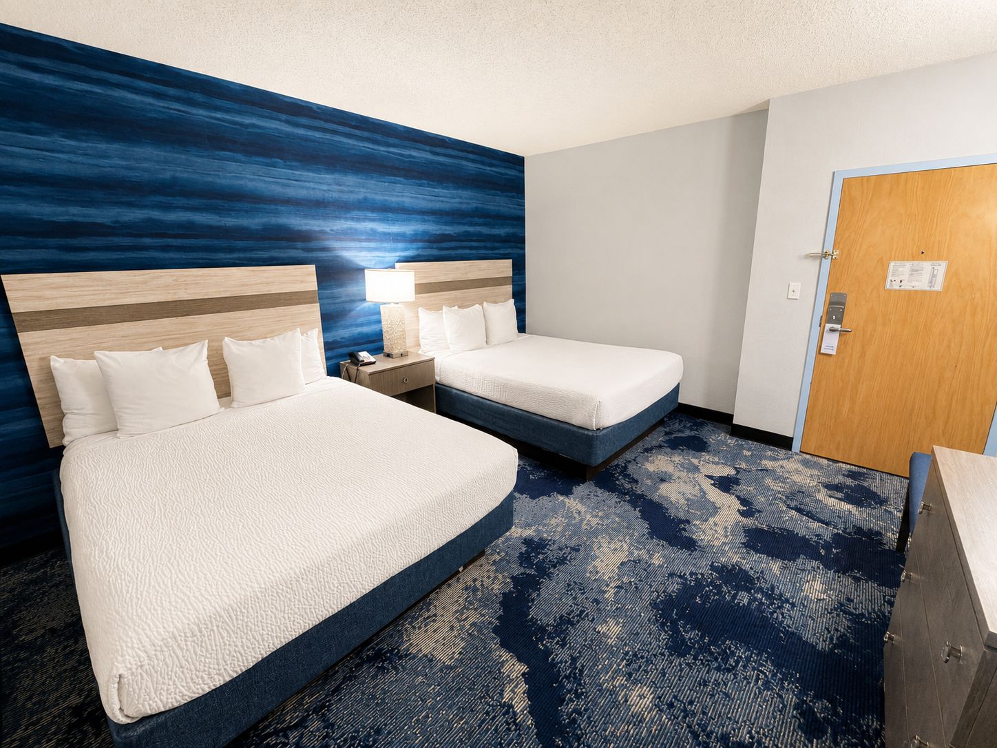A hotel room with two beds, a nightstand, a lamp, and a door with a sign.