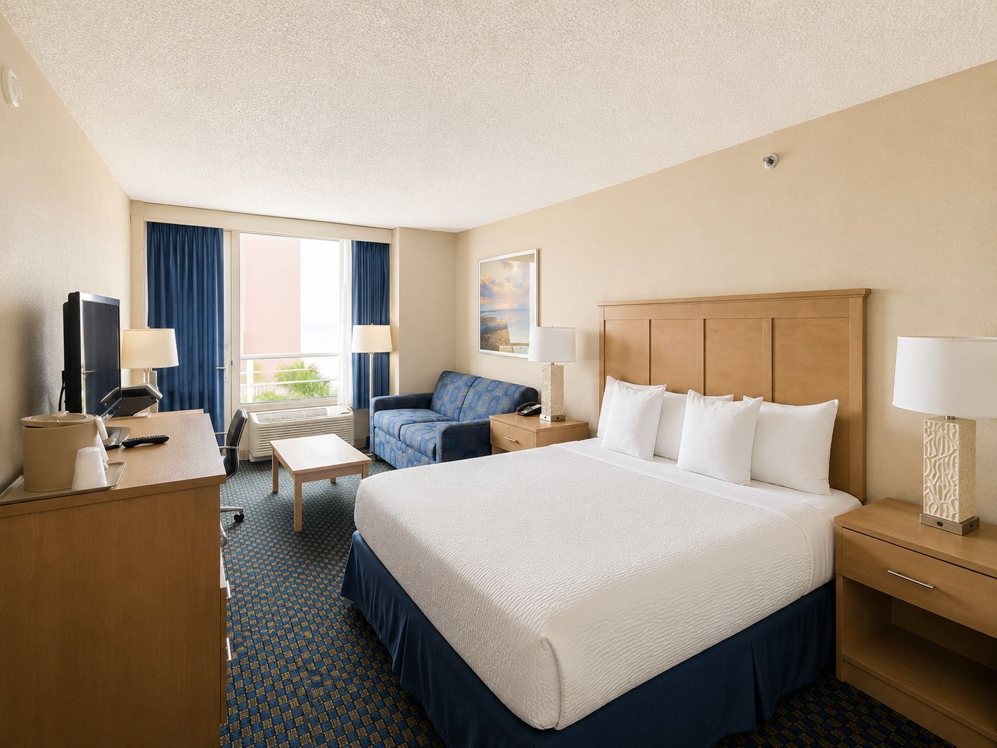 Une chambre d’hôtel avec un grand lit, un bureau, une chaise, un canapé et une fenêtre avec des rideaux.