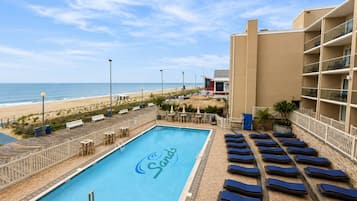 A swimming pool with lounge chairs and a view of the beach.