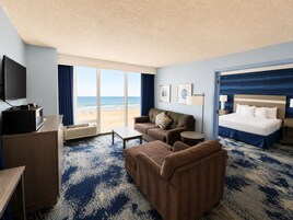A hotel room with a large bed, a sofa, a television, and a view of the beach.