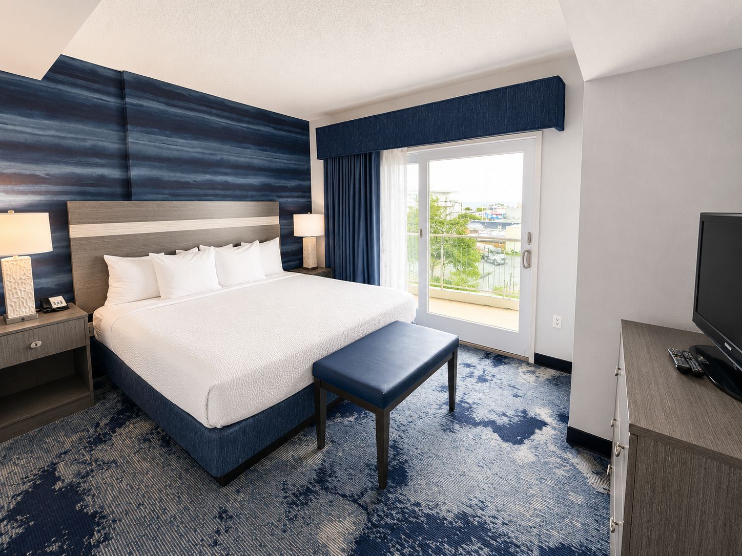 Une chambre d’hôtel avec un grand lit, un banc, une télévision et une vue sur l’extérieur.