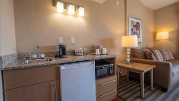 Una habitación de hotel compacta con kitchenette, una mesa de comedor, un sofá y una lámpara.