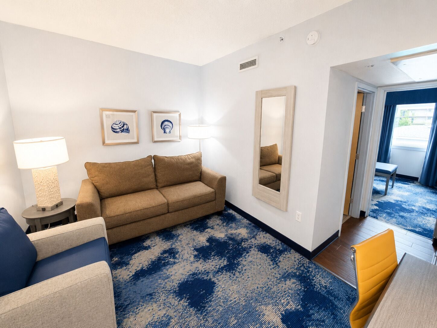 Une chambre d’hôtel avec un canapé, un fauteuil, une lampe, un miroir et une vue sur l’extérieur.
