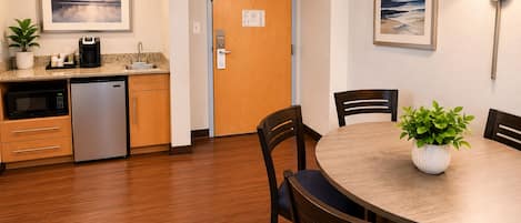 Una cocina compacta con microondas, refrigerador y pileta, un comedor con mesa y sillas, y dos cuadros en las paredes.