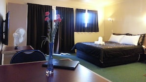 A hotel room with a bed, a desk with a laptop, a vase with flowers, and a television. - New Castle Motor Lodge (Rotorua)