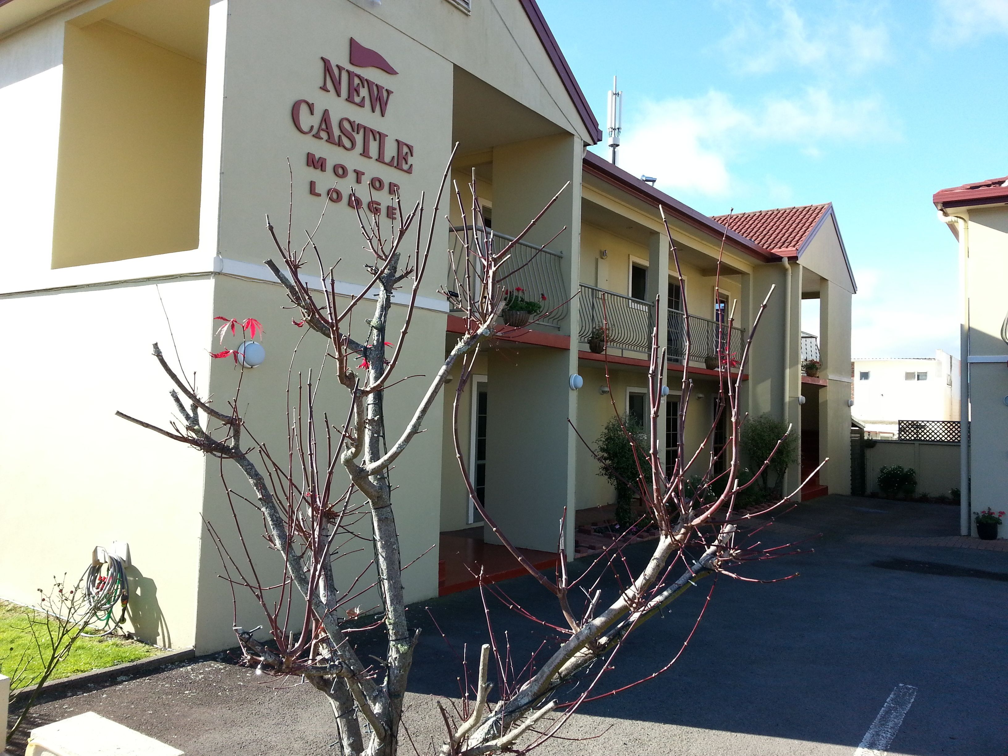 A building labeled "New Castle Motor Lodge" with a balcony and a clear sky.
