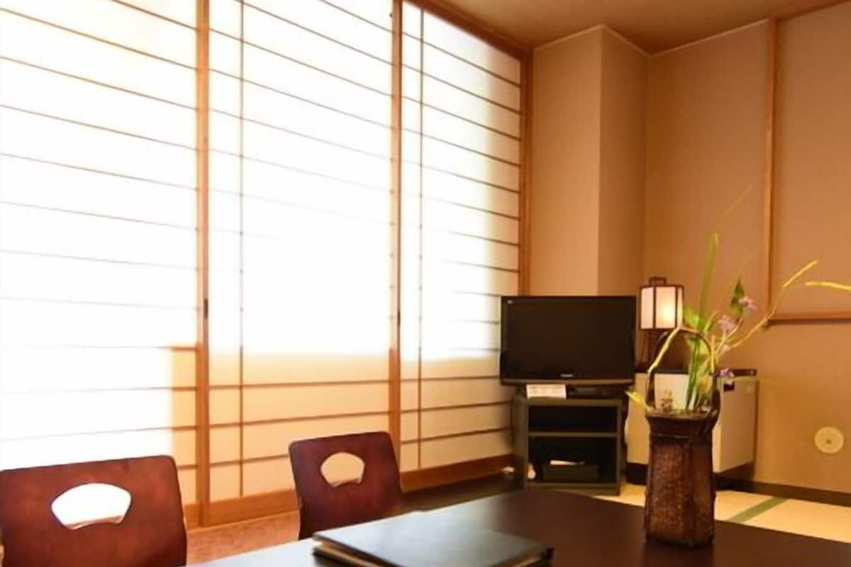 A room with a dark wooden table, two chairs, a television on a stand, and a vase with flowers.